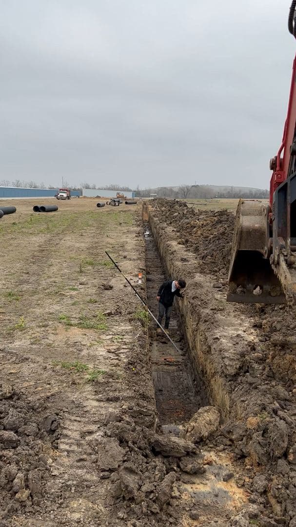 Excavating a long drainage trench across an open lot